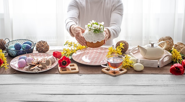 Easter composition with cake in female hands, tea, flowers, eggs and decor details. Easter family holiday concept.