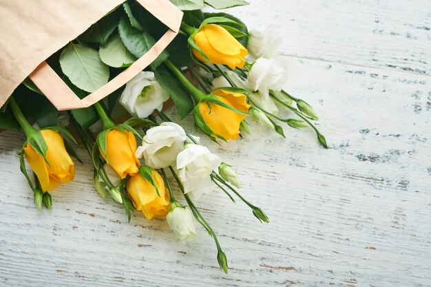 Easter concept Bouquet of fresh white and yellow roses in paper bag on old white wooden background Passover Pesah celebration concept Concept of mothers day womens day spring background Top view