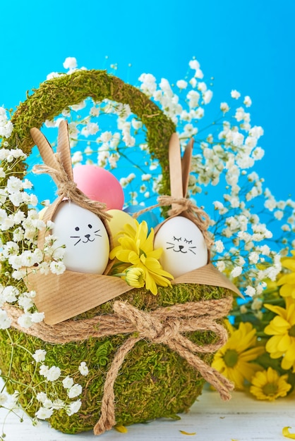 Photo easter concept. eggs in basket decorated with flowers on a blue background