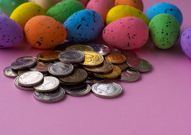 Easter concept with coins and colorful eggs on pink background