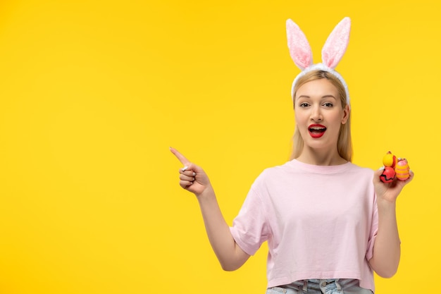 Easter cute young blonde girl wearing pink bunny ears holding colorful eggs and smiling