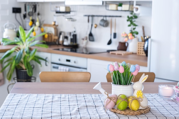 Easter decoration of colorful eggs in a basket and a rabbit on the kitchen table in a rustic style Festive interior of a country house