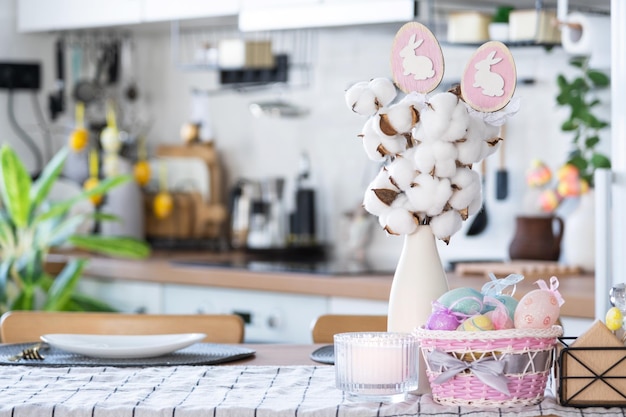 Easter decoration of colorful eggs in a basket and a rabbit on the kitchen table in a rustic style Festive interior of a country house