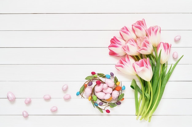 Easter decoration. Decorative Easter eggs and pink tulips on white wall Copy space, top view.