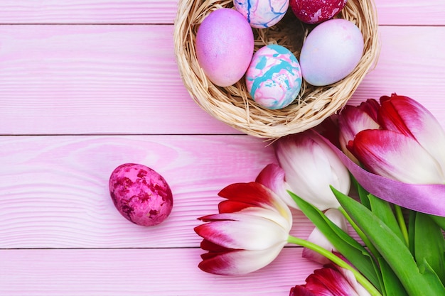 Easter decoration with colorful eggs and  tulips over pink wood. Top view with copy space