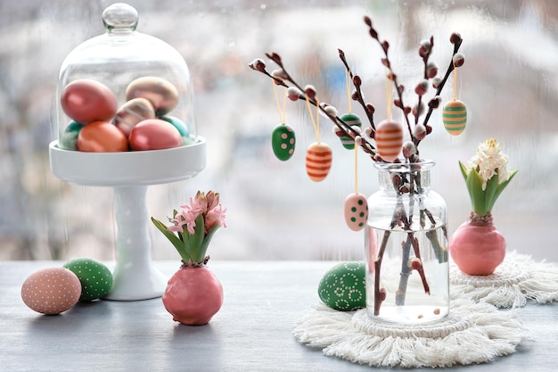 Easter decorations on window sill in Spring Wooden painted eggs on pussy willow twigs in glass bottle Hyacinth flowers bulbs in pink wax Window with urban view Romantic indoor setup Happy Easter