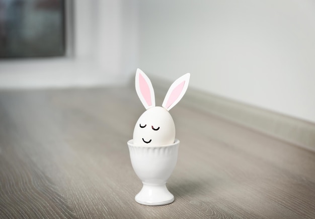 Easter egg with paper ears in cup on table