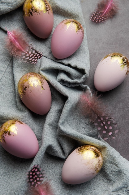 Easter eggs are painted with violet and gold paint on a gray linen background