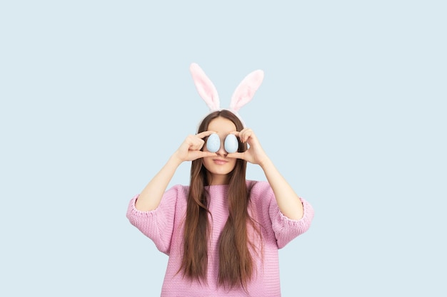 Easter eggs background holiday discounts and sales concept Happy girl in the bunny ears with decorated eggs smiling isolated on a blue background in studio