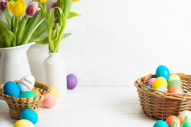 Easter eggs in baskets and yellow tulips bouquet in vase near wall