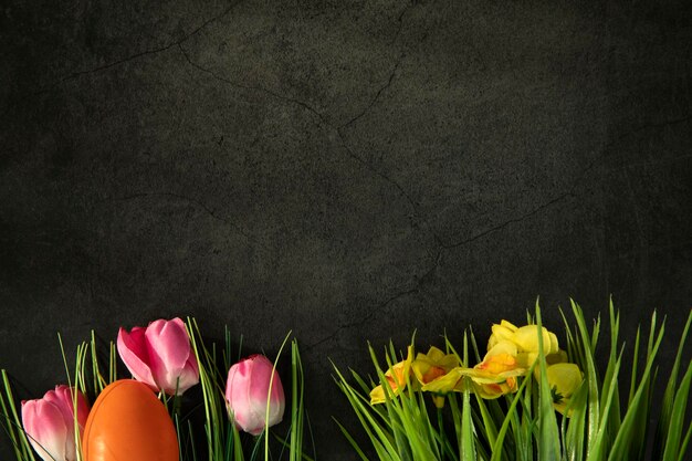 Easter eggs on fresh green grass against grey concrete background colorful pink tulips and yellow da