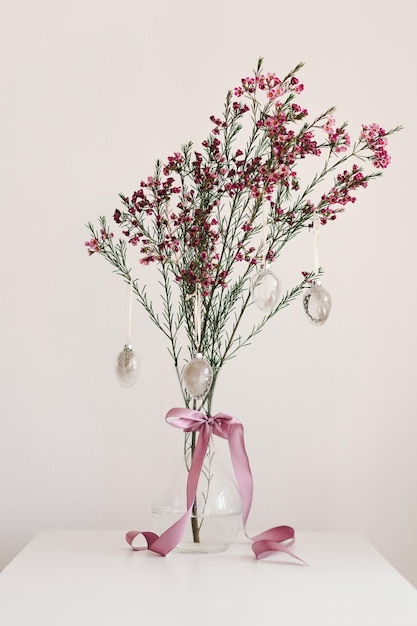 Easter eggs hang on a sprig of flowers in a transparent vase Spring and Easter concept