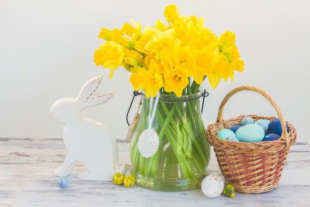 Easter eggs hunt white rabbit basket with painted blue eggs and daffodils bouquet