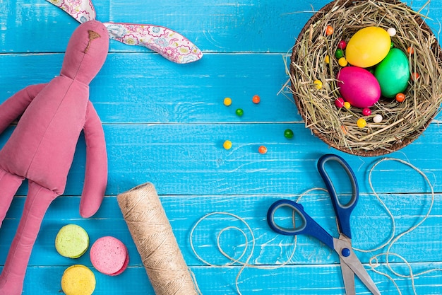 Easter eggs in nest and rabbit on blue rustic wooden planks