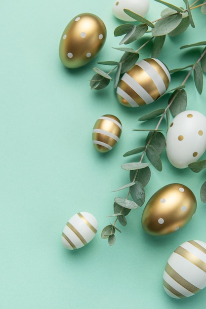 Easter eggs painted in gold and eucalyptus branches on a soft green background