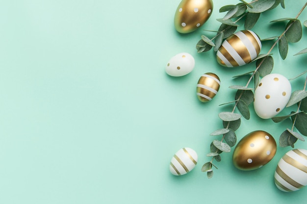 Easter eggs painted in gold and eucalyptus branches on a soft green background