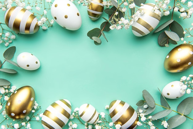 Easter eggs painted in gold and eucalyptus branches on a soft green background