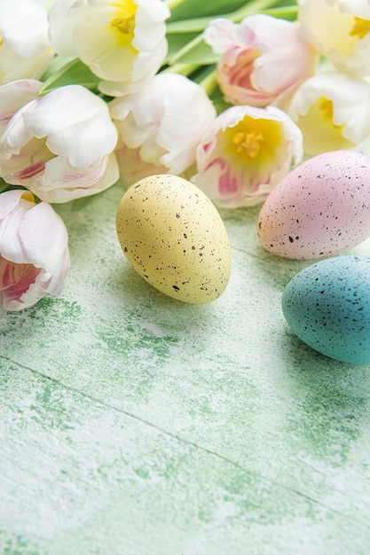 Easter eggs painted pastel colors and pink tulips on a green wooden background