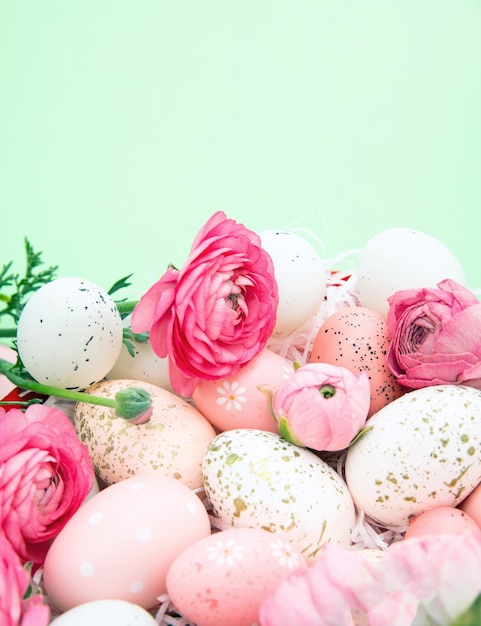 Easter eggs and pink buttercups flower bouquet on pastel green background copy space