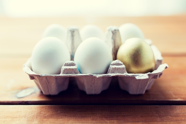 easter, food, cooking and object concept - close up of white and golden eggs in egg box or carton wooden surface