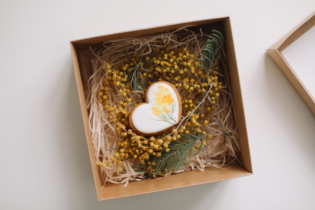 Easter gingerbread cookie in shape of a heart in a gift box with colorful yellow mimosa flowers Eastet Spring April card or banner Top view