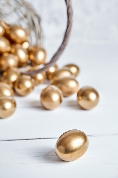 Easter golden eggs spilled out of wicker basket on white wooden table