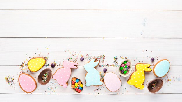 Easter greetings card with colorful gingerbread and sweets On a white wooden background Top view Free space for your text