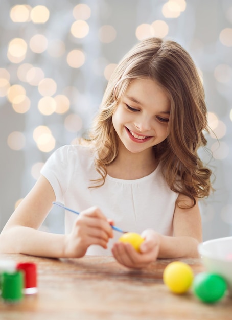 easter, holiday and child concept - close up of girl with brush coloring easter eggs over lights background