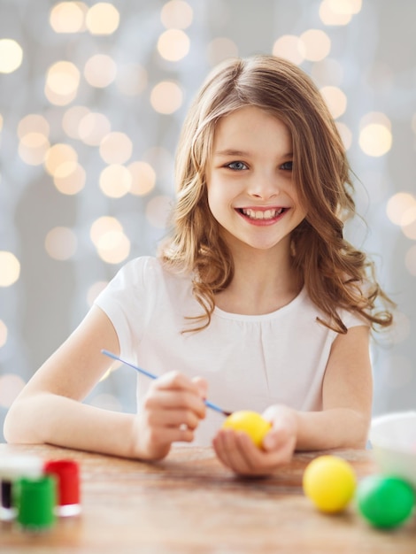 easter, holiday and child concept - close up of girl with brush coloring easter eggs over lights background