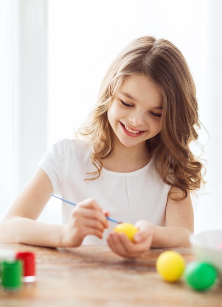 easter, holiday and child concept - smiling little girl coloring eggs for easter