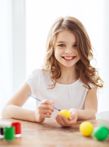 easter, holiday and child concept - smiling little girl coloring eggs for easter