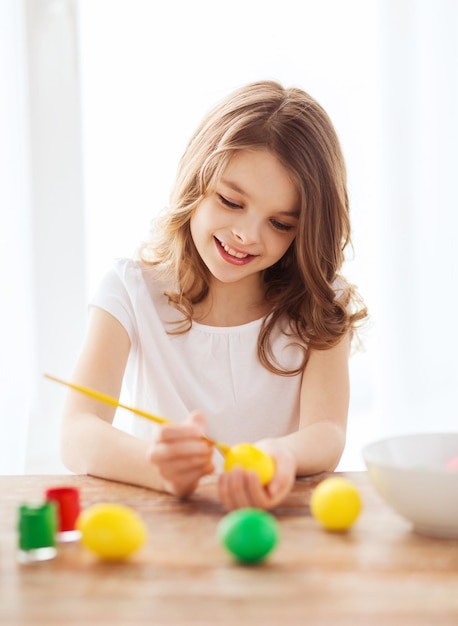 easter, holiday and child concept - smiling little girl coloring eggs for easter