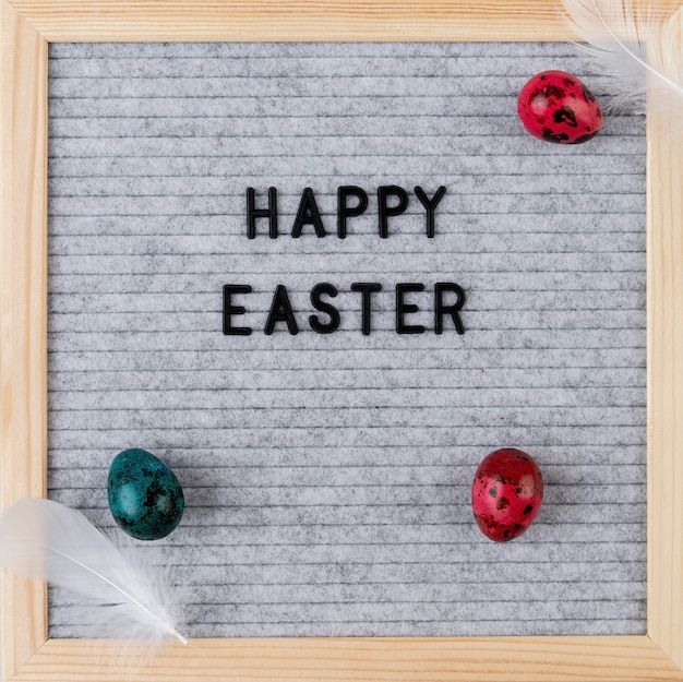 Easter holiday concept. The words Happy Easter on grey felt letter board decorated with quail eggs and feathers