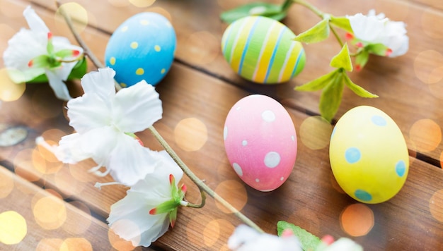 easter, holidays, spring, tradition and object concept - close up of colored easter eggs and flowers on wooden surface