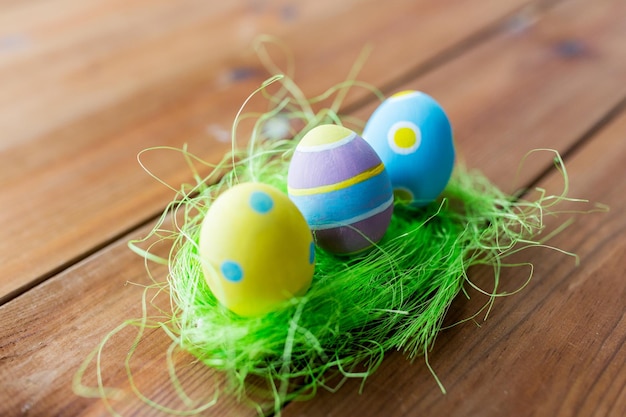 easter, holidays, tradition and object concept - close up of colored easter eggs and decorative grass on wooden surface