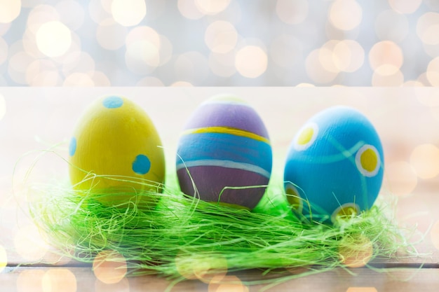 easter, holidays, tradition and object concept - close up of colored easter eggs and decorative grass on wooden surface