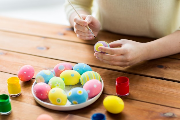 easter, holidays, tradition and people concept - close up of woman hands coloring easter eggs with colors and brush