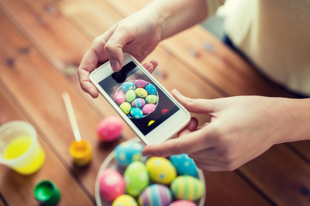 easter, holidays, tradition, technology and people concept - close up of woman hands with smartphone taking picture of colored easter eggs