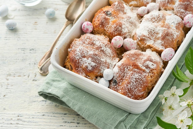 Easter Hot cross buns Traditional Easter treats cross buns with raisins butter chocolate candy eggs with blossoming cherry or apple flowers on rustic light wooden backgrounds Easter holiday meal