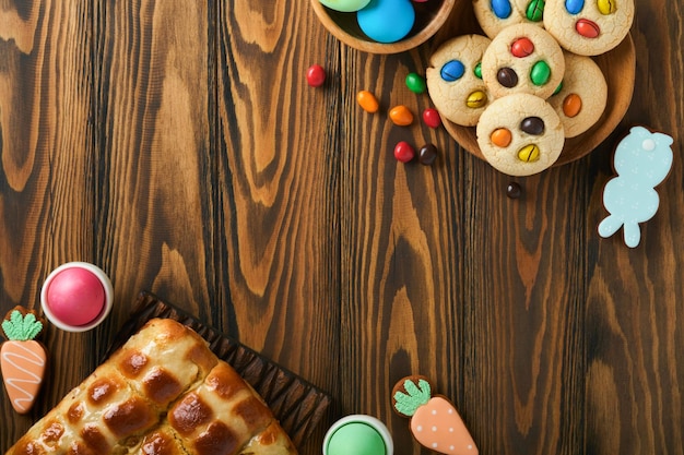 Easter hot cross buns with colored eggs Easter gingerbread rabbits and cookies over dark brown plank wooden old table background Spring holiday baking concept Easter table setting Top view Mock up