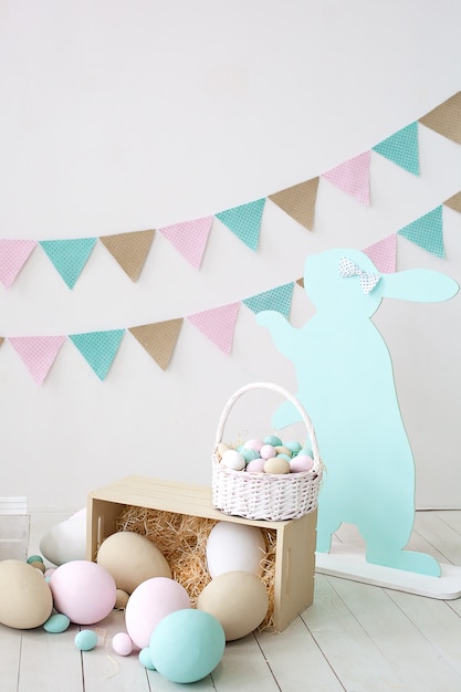 Easter! A lot of colorful Easter eggs! Easter decoration of a room with rabbits and baskets with eggs. Farm. harvesting. Basket with carrots and bunnies. Easter decor. Holiday flags on white wall