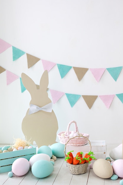 Easter! A lot of colorful Easter eggs! Easter decoration of a room with rabbits and baskets with eggs. Farm. harvesting. Basket with carrots and bunnies. Easter decor. Holiday flags on white wall