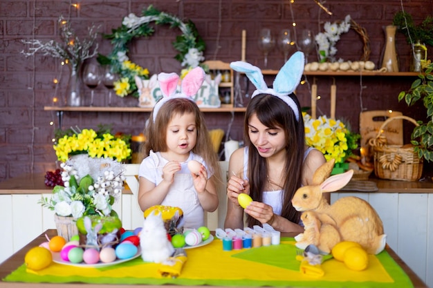 Easter mom and daughter paint Easter eggs with paint smile and prepare for the holiday at home in the kitchen in the ears of a hare