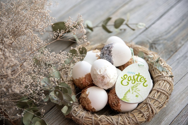 Easter still life with decorated Easter eggs and decorative nest on a wooden surface with dry twigs. Happy Easter wishes concept.