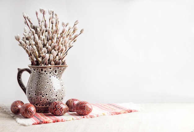 Easter still life with Pysanka and willow branches in ceramic jug on traditional Ukrainian cloth. Decorated Easter eggs, traditional for Eastern Europe culture