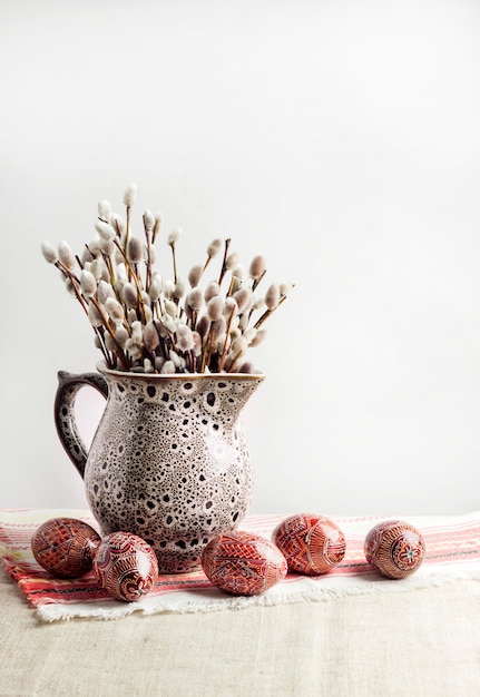 Easter still life with Pysanka and willow branches in ceramic jug on traditional Ukrainian cloth. Decorated Easter eggs, traditional for Eastern Europe culture