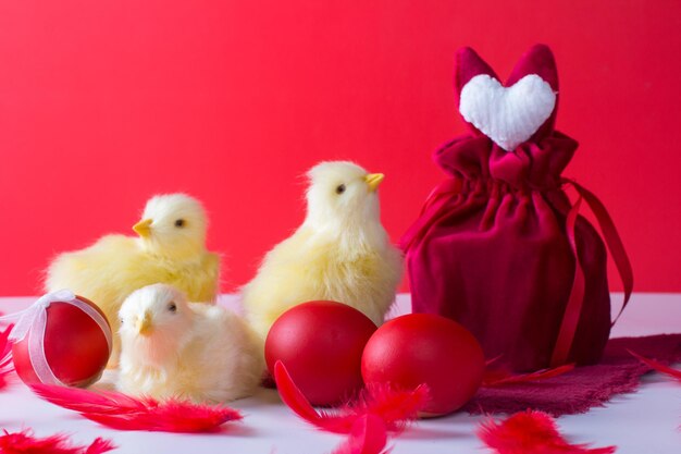 Easter still life with a white rabbit and chickens on a red background A wine glass and painted eggs the concept of the bright Easter holiday