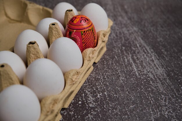 Easter table setting festive composition. White eggs and one decorated in carton box on grey table. copy text space.