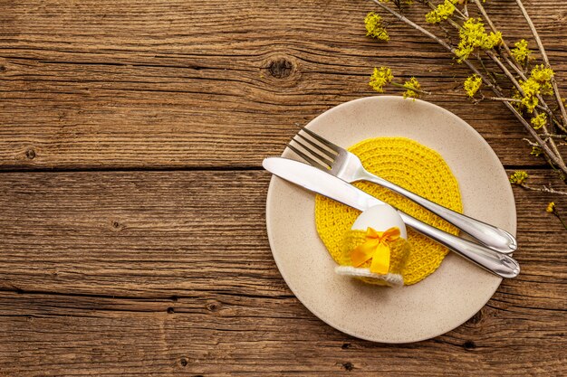 Easter table setting on old wooden background. Spring holiday card template. Cutlery, crochet napkin, egg, flowering sprigs of dogwood