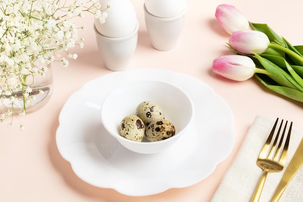 Easter table setting in pink color Chicken and quail eggs white dishware golden cutlery flowers